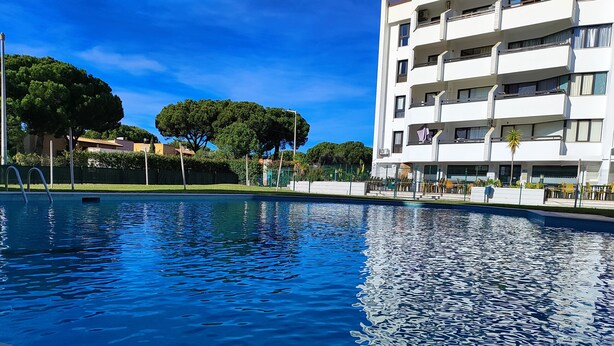 A swimming pool with clear blue water, surrounded by a fence, and adjacent to a multi-story building with balconies. - Vilamoura Charming With Pool by Homing (Loulé)