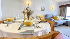 A dining area with a round table set for four, a sofa in the background, and a mirror on the wall. - Vilamoura Charming With Pool by Homing (Loulé)