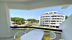 A balcony with a white table and chairs, a clear view of a multi-story building, and a green landscape with trees. - Vilamoura Charming With Pool by Homing (Loulé)