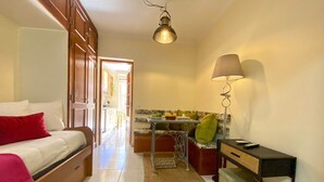 A compact room with a bed, a desk, a lamp, and a kitchenette.