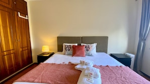 Una camera d'albergo con un letto, un comodino con una lampada, un armadio in legno e una finestra con tende.