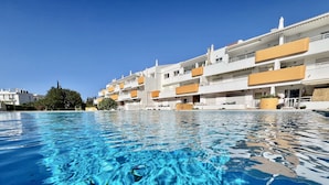 Una piscina limpida con vista su un edificio di un hotel multipiano con balconi e cielo sereno.