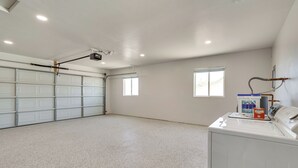 A spacious laundry room with a large white washing machine, a ceiling-mounted projector, and a garage door. - Patio + Private Casita: Lake Havasu City Home! (Lake Havasu City)