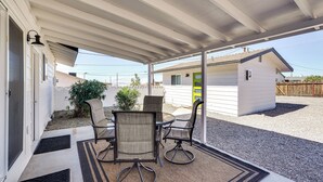 A covered patio with a table and chairs, a small shed, and a house in the background. - Patio + Private Casita: Lake Havasu City Home! (Lake Havasu City)