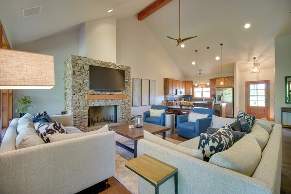 A spacious living room with a stone fireplace, a large flat-screen TV, and a dining area with wooden cabinets and a kitchen in the background. - Pool Access, Deck & Boat Slip: Monkey Island Oasis (Afton)