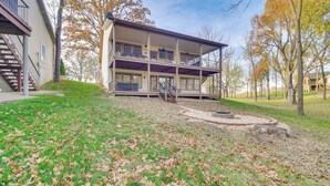 A two-story building with a balcony on the upper floor, a fire pit in the front yard, and trees with autumn leaves in the background.