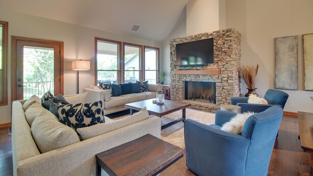 A spacious living room with a stone fireplace, comfortable seating, and large windows.