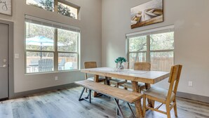 A dining area with a wooden table, benches, and chairs. There are large windows providing natural light and a view of the outdoors. - Modern Canyon Lake Vacation Home w/ Furnished Deck (Canyon Lake)