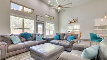 A spacious living room with leather sofas, a large ottoman, and a ceiling fan.