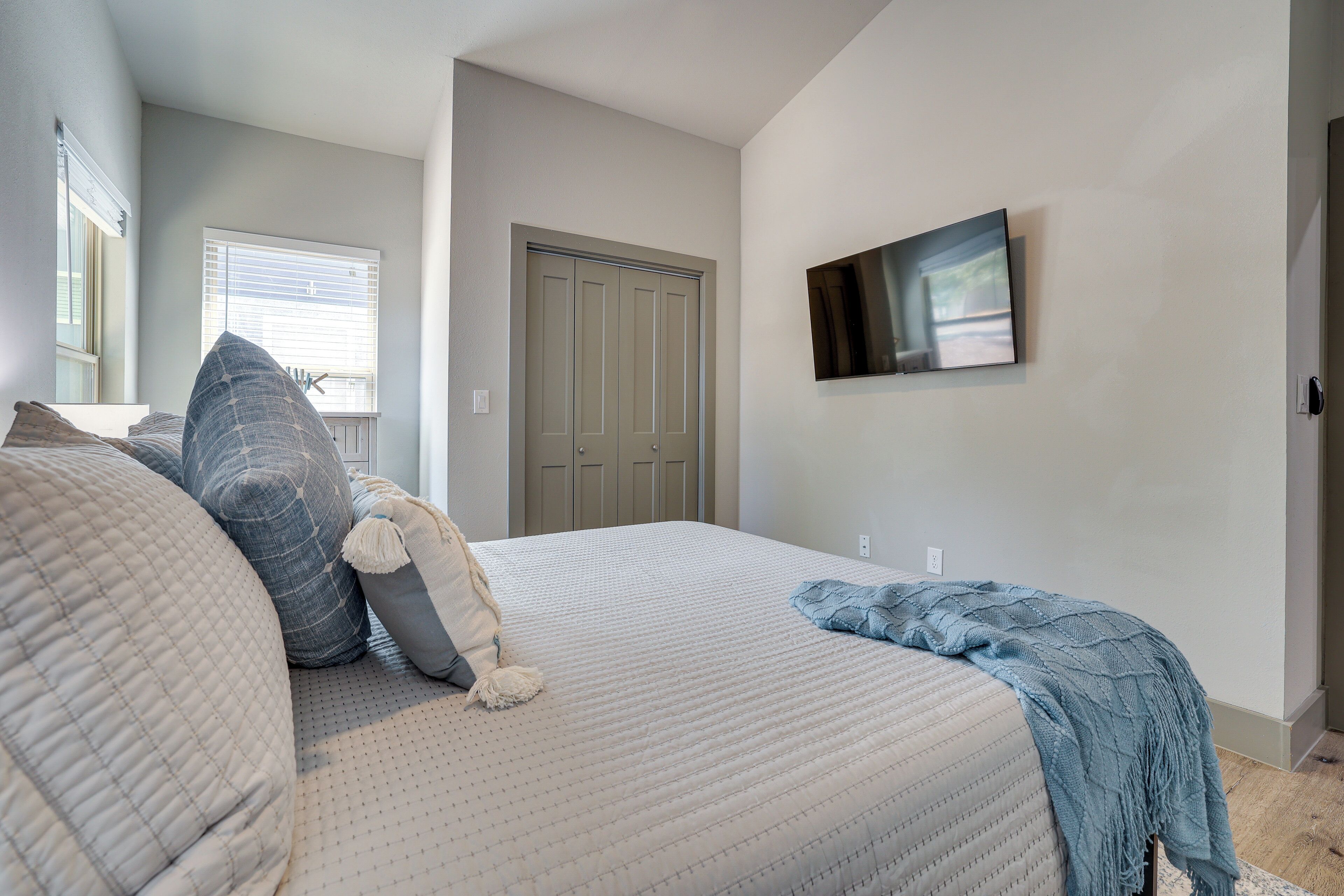 A bedroom with a bed, pillows, a blanket, a TV on the wall, and a door.