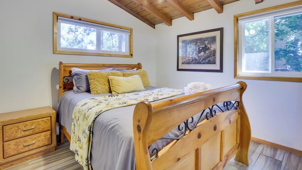 A bedroom with a wooden bed, two bedside tables, a window, and a framed picture on the wall. - Pet-friendly Big Bear Cabin, Near Hiking & Skiing! (Big Bear City)
