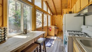 A cabin kitchen with a stove, sink, and large windows overlooking a forest. - Pet-friendly Big Bear Cabin, Near Hiking & Skiing! (Big Bear City)