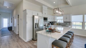 Een moderne keuken met witte kasten, roestvrijstalen apparatuur en een groot kookeiland met barstoelen.