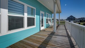 Een houten terras met een turquoise gevel en witte accenten, dat uitkomt op een overdekte veranda.