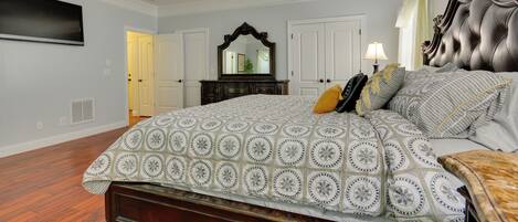 A bedroom with a large bed, a ceiling fan, a flat-screen TV, a dresser, and a mirror.