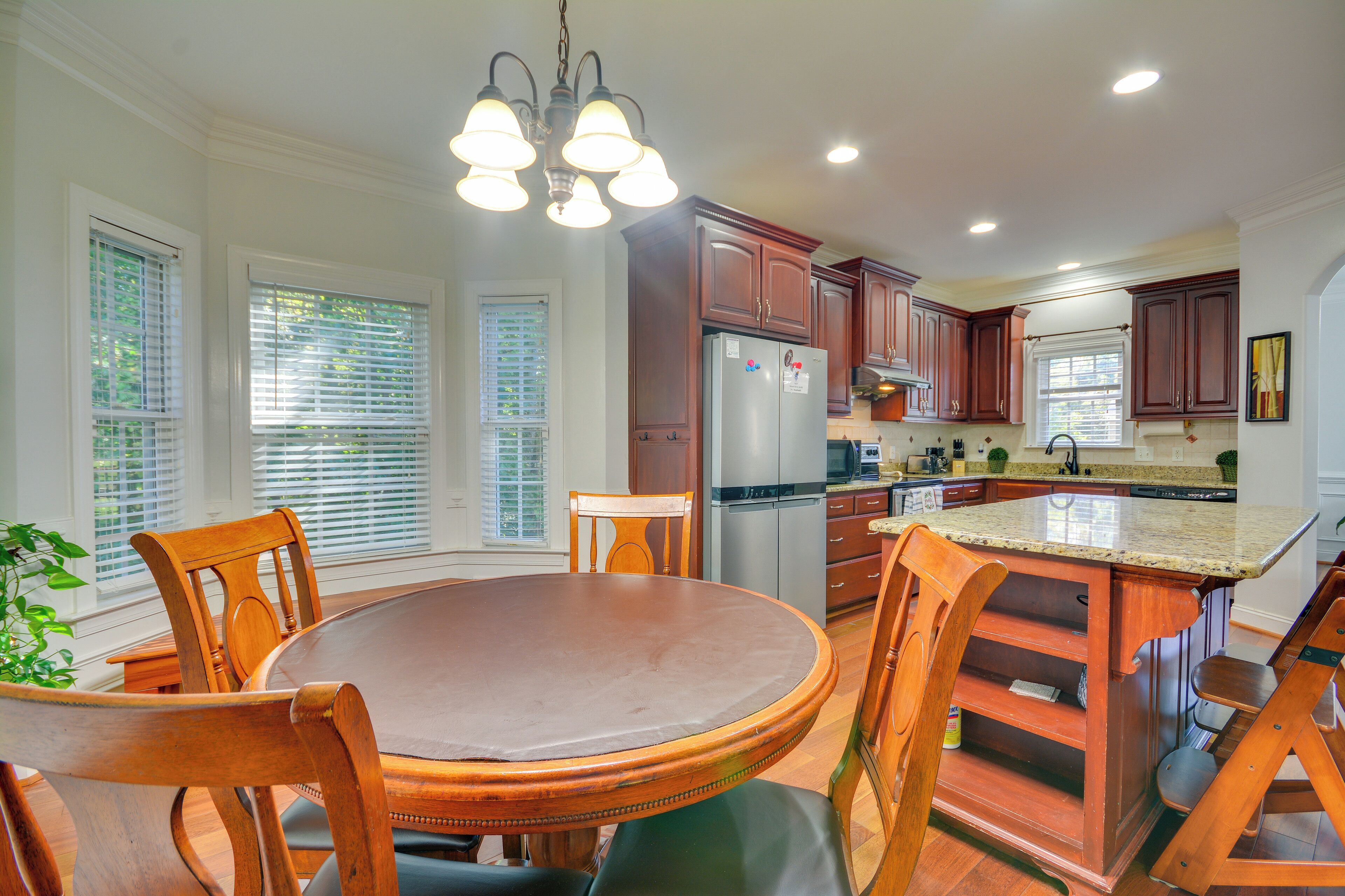 A kitchen with wooden cabinets, a stainless steel refrigerator, and a dining area with a round table and chairs.