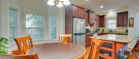 A kitchen with wooden cabinets, a stainless steel refrigerator, and a dining area with a round table and chairs.