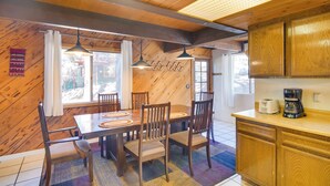 A wooden interior with a dining table, chairs, and a kitchen area including cabinets and a coffee maker. - Quaint Big Bear Home w/ Hot Tub: 4 Mi to Skiing! (Big Bear City)