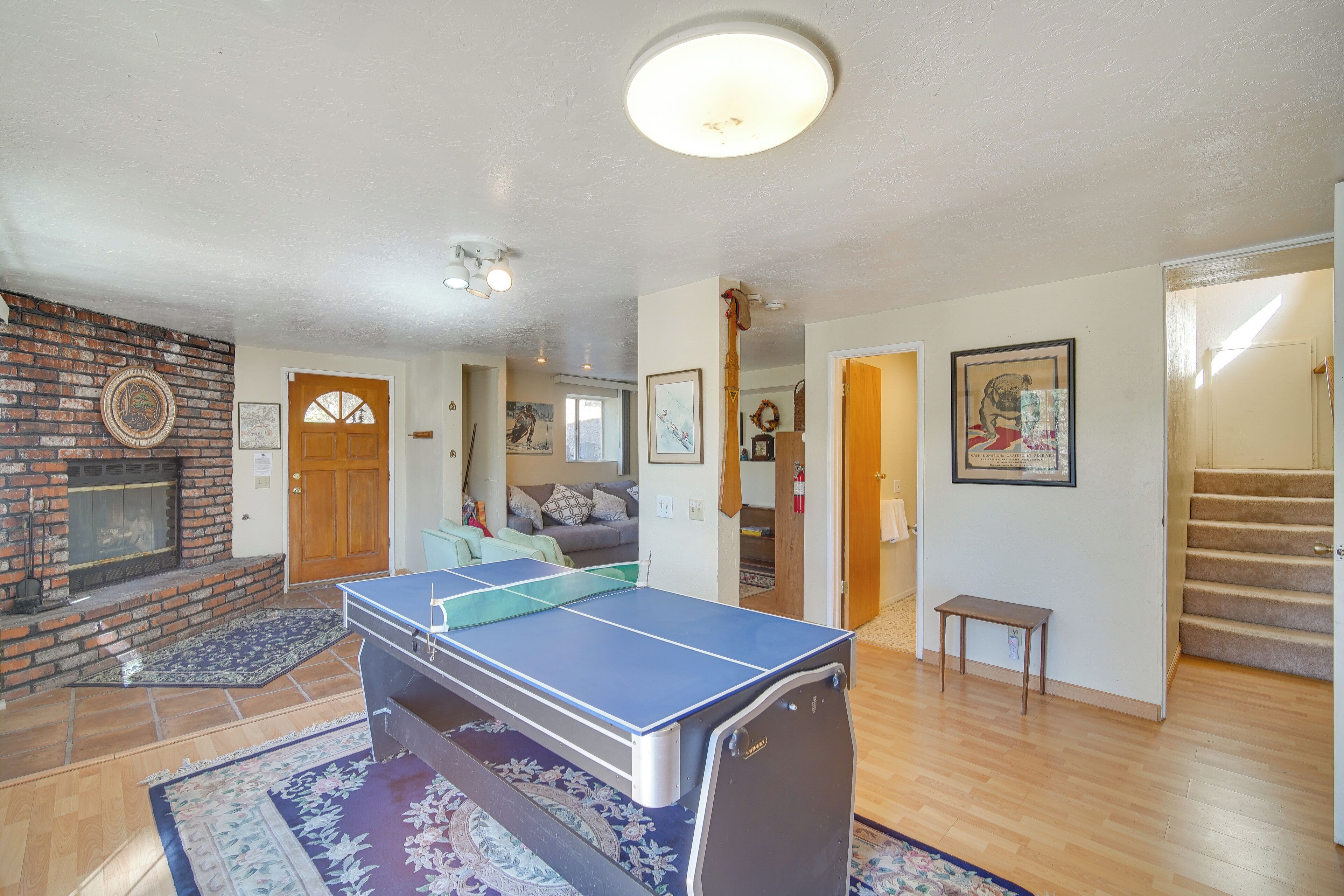 A living room with a ping pong table, a fireplace, and a staircase.