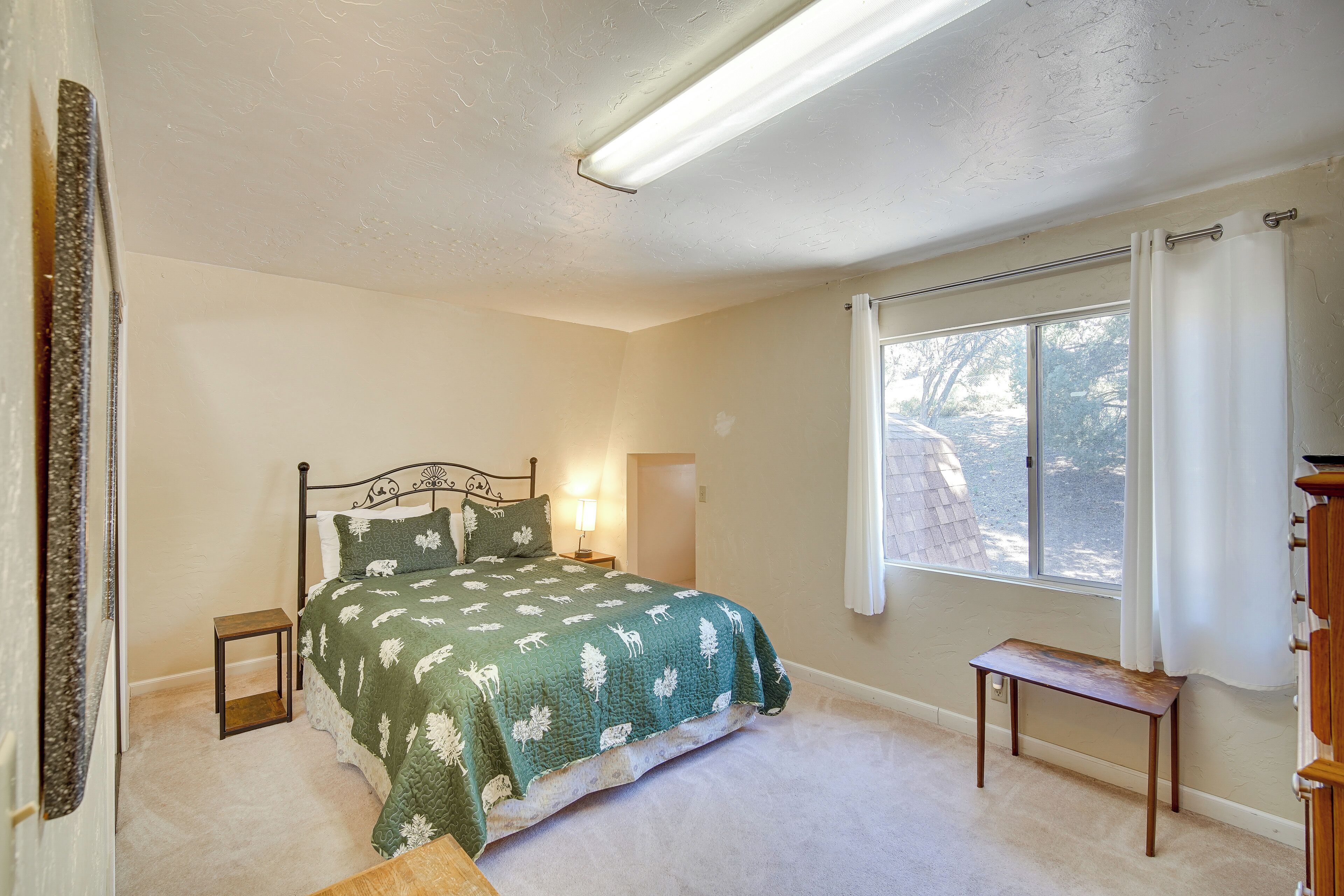 A bedroom with a bed, bedside tables, a window, and a view of the outdoors.