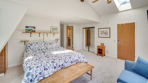 A bedroom with a bed, a bench, a blue sofa, a ceiling fan, a skylight, and a door. - Quaint Big Bear Home w/ Hot Tub: 4 Mi to Skiing! (Big Bear City)