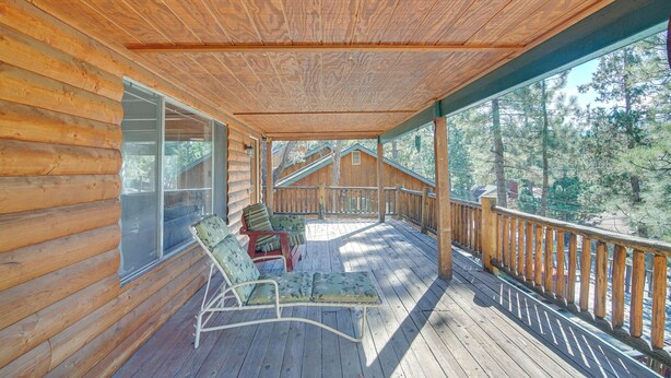 A wooden cabin with a covered porch, two lounge chairs, and a view of a forest. - Quaint Big Bear Home w/ Hot Tub: 4 Mi to Skiing! (Big Bear City)