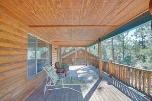 A wooden cabin with a covered porch, two lounge chairs, and a view of a forest. - Quaint Big Bear Home w/ Hot Tub: 4 Mi to Skiing! (Big Bear City)