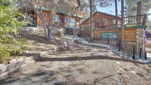 A rustic cabin with a stone staircase leading to a wooden deck, surrounded by trees. - Quaint Big Bear Home w/ Hot Tub: 4 Mi to Skiing! (Big Bear City)