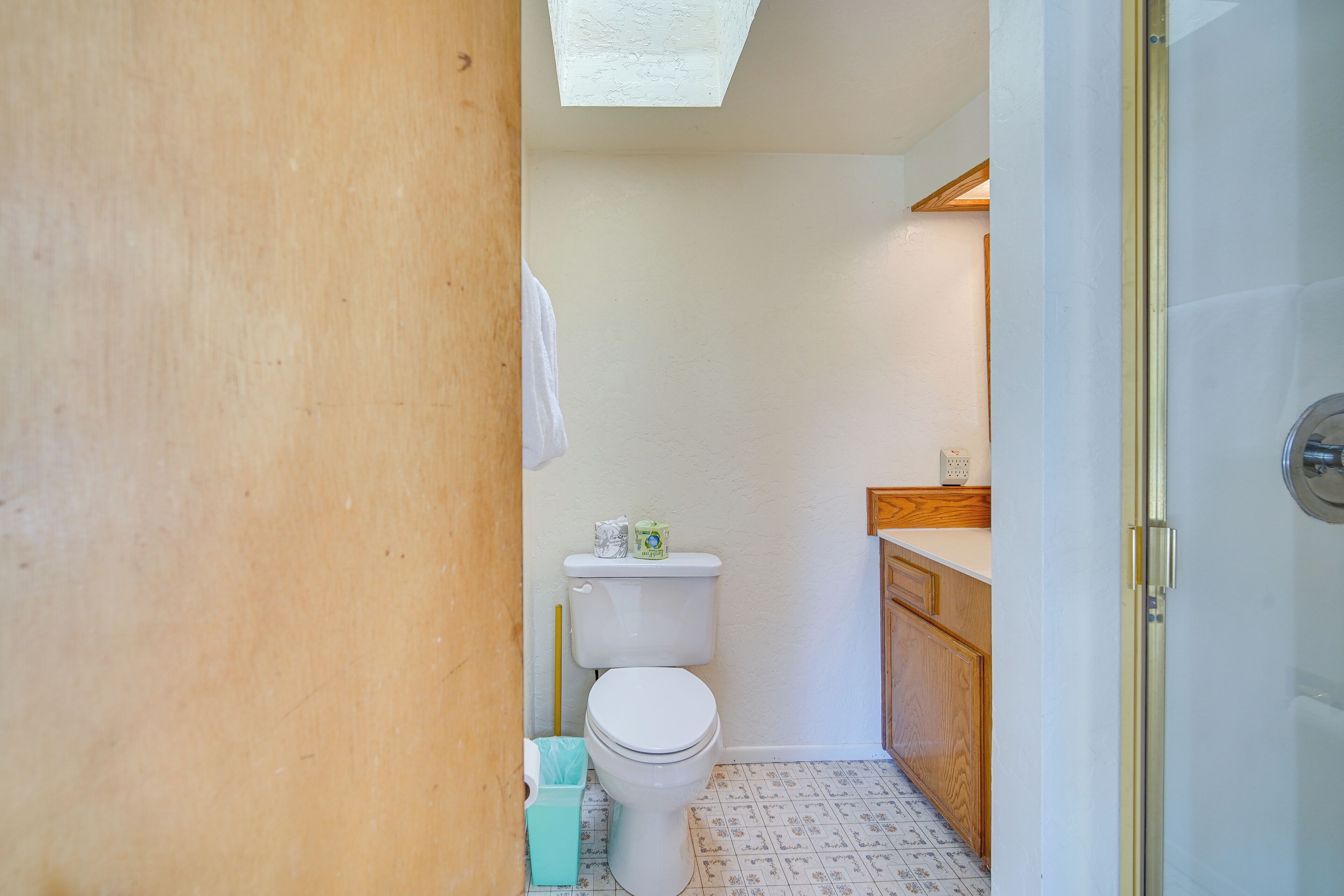 Un baño pequeño con un inodoro, un cubo de basura y un armario de madera.