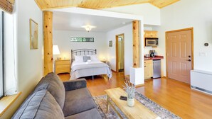 A cozy room with a bed, a sofa, a wooden ceiling, a kitchen area, and a door.