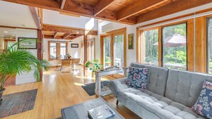 A spacious living area with a wooden ceiling, large windows, a gray sofa with floral cushions, and a dining area in the background. - Ellsworth Home ~ 18 Mi to Acadia Nat'l Park! (Ellsworth)