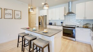 A modern kitchen with white cabinets, stainless steel appliances, and a central island with bar stools. - Modern Livingston Condo Near Yellowstone River! (Livingston)