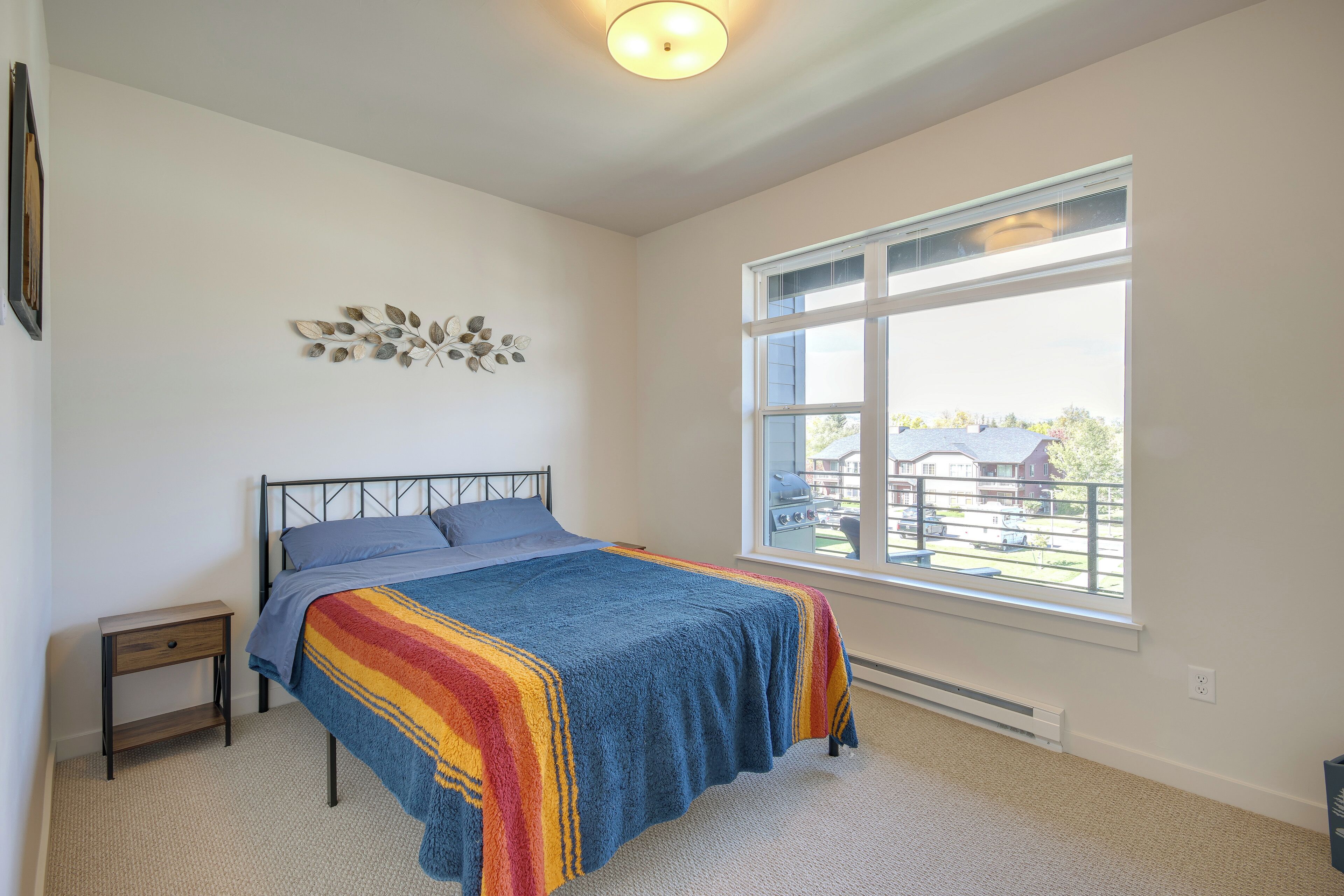 A bedroom with a bed, a nightstand, a window with a view, and a ceiling light.