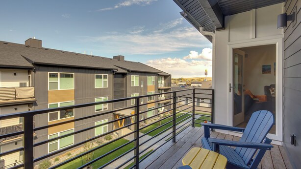 A balcony with a blue chair and a small table, overlooking a residential area with multiple buildings. - Modern Livingston Condo Near Yellowstone River! (Livingston)