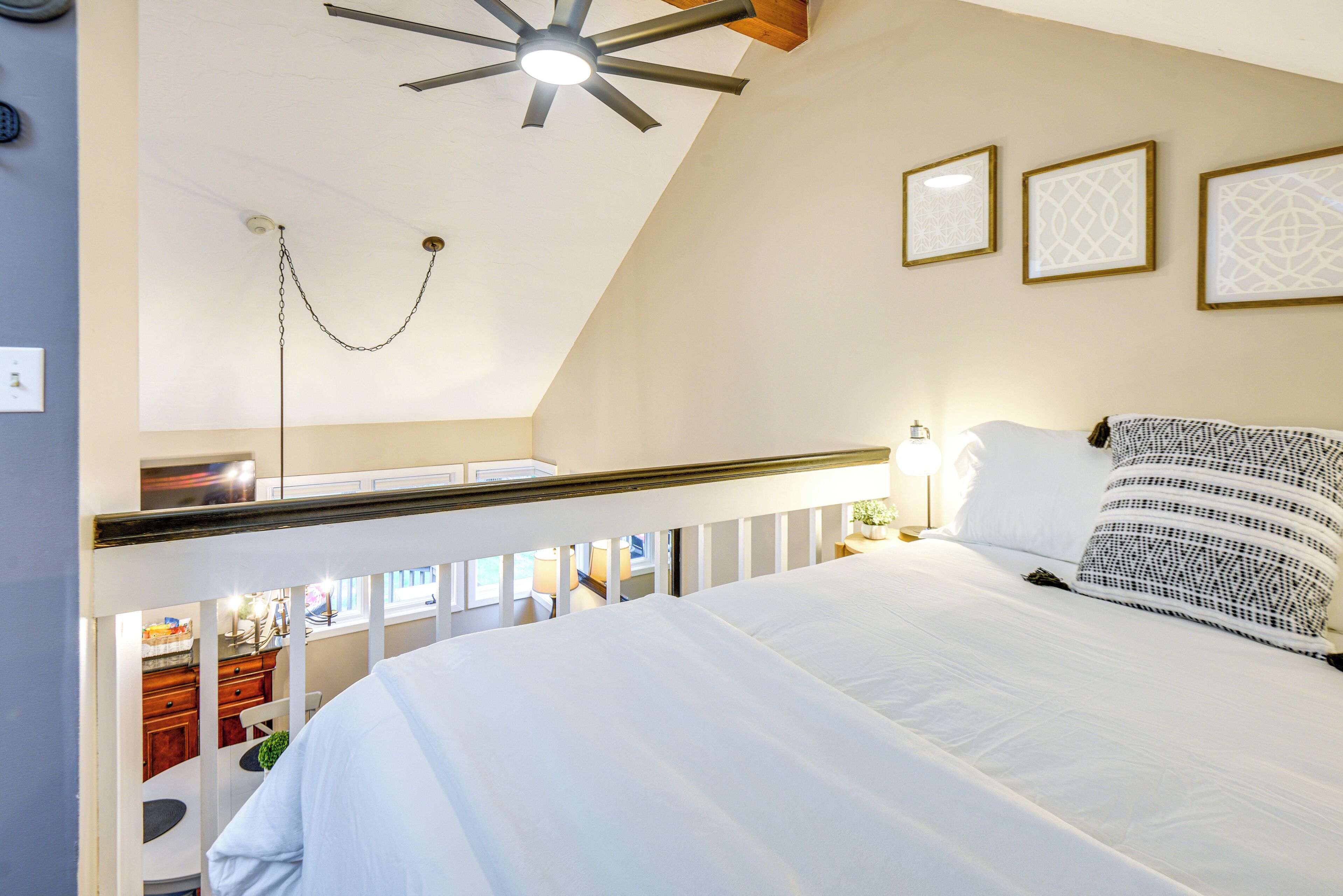 A bedroom with a bed, a ceiling fan, and three framed pictures on the wall.