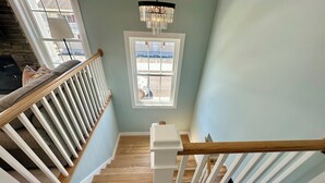 Una escalera con barandas blancas y peldaños de madera, que conduce a una plataforma con ventana y una araña.