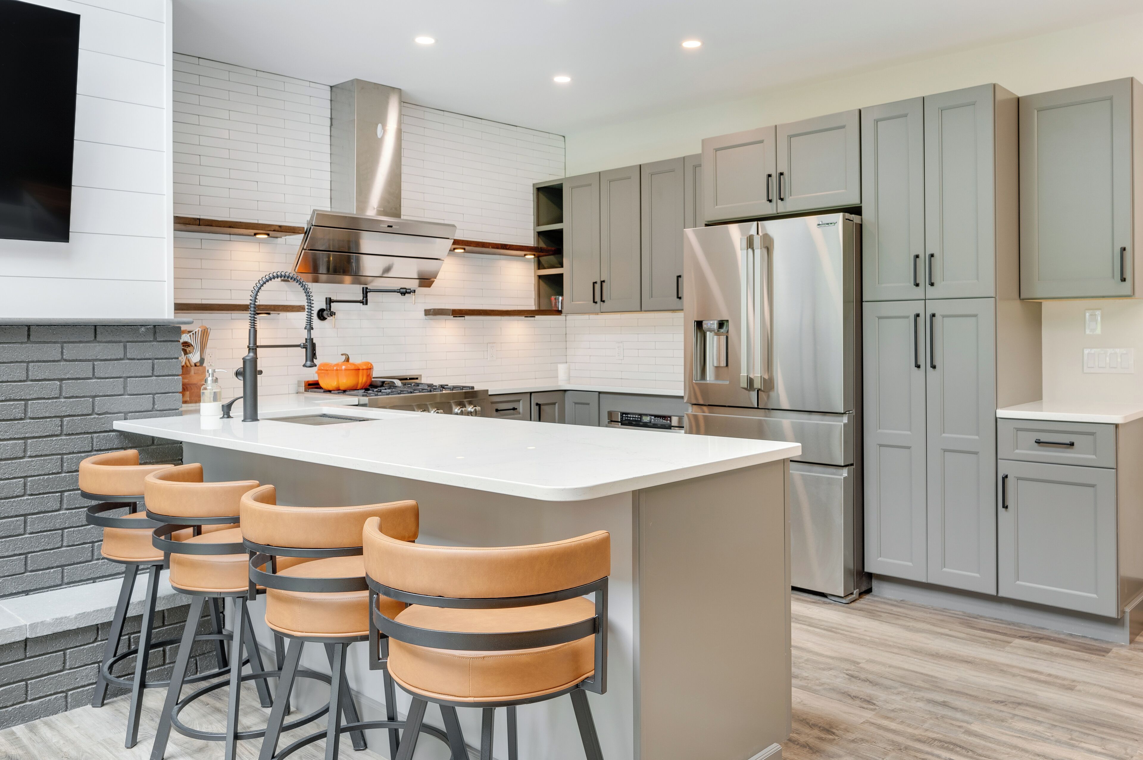 A modern kitchen with a central island, bar stools, stainless steel appliances, and light grey cabinetry.