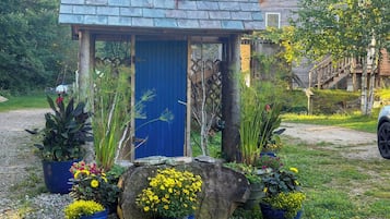 A rustic wooden structure with a blue door, surrounded by various potted plants and a stone.