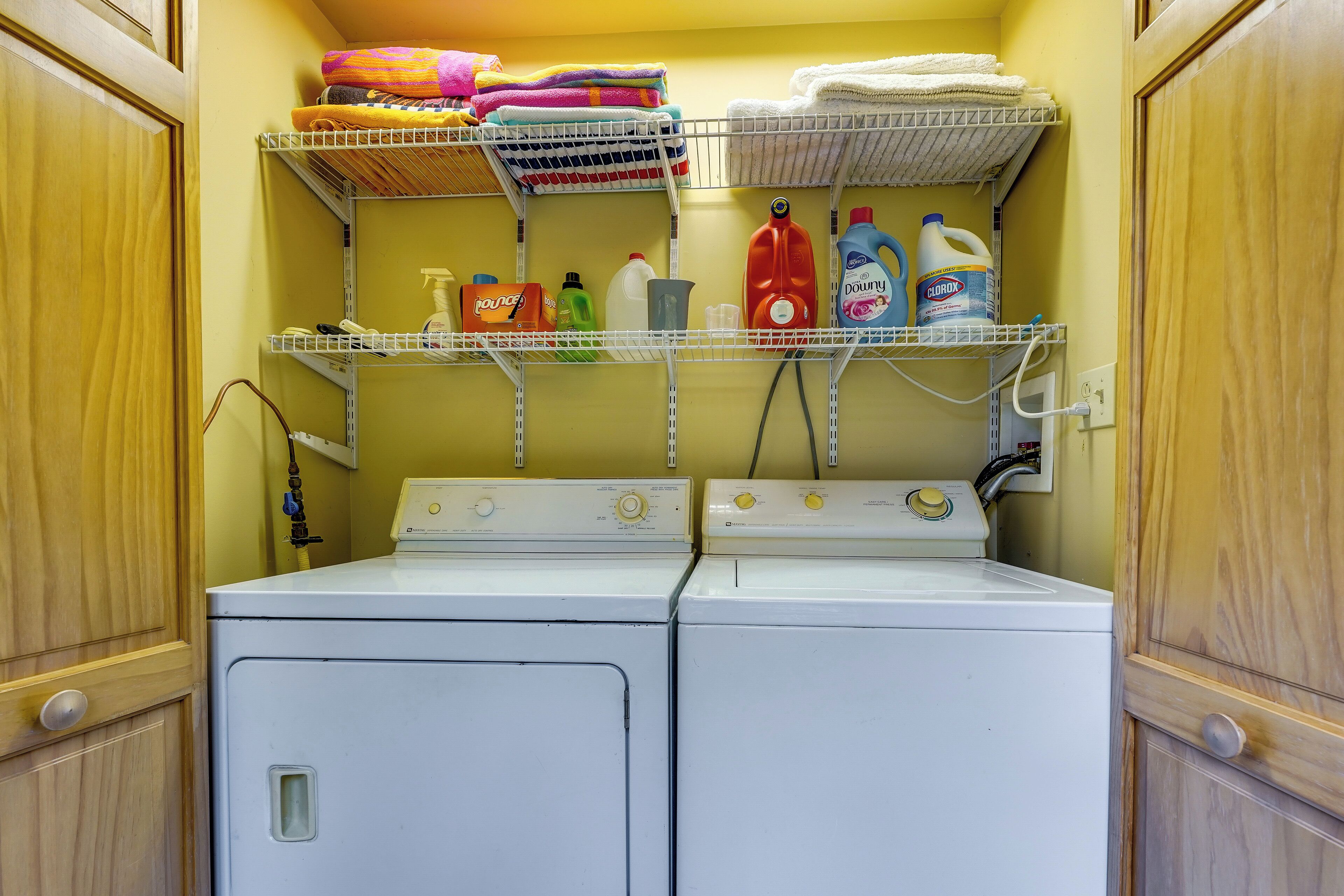 Een wasserette met twee witte wasmachines, planken met gevouwen handdoeken en diverse schoonmaakmiddelen.