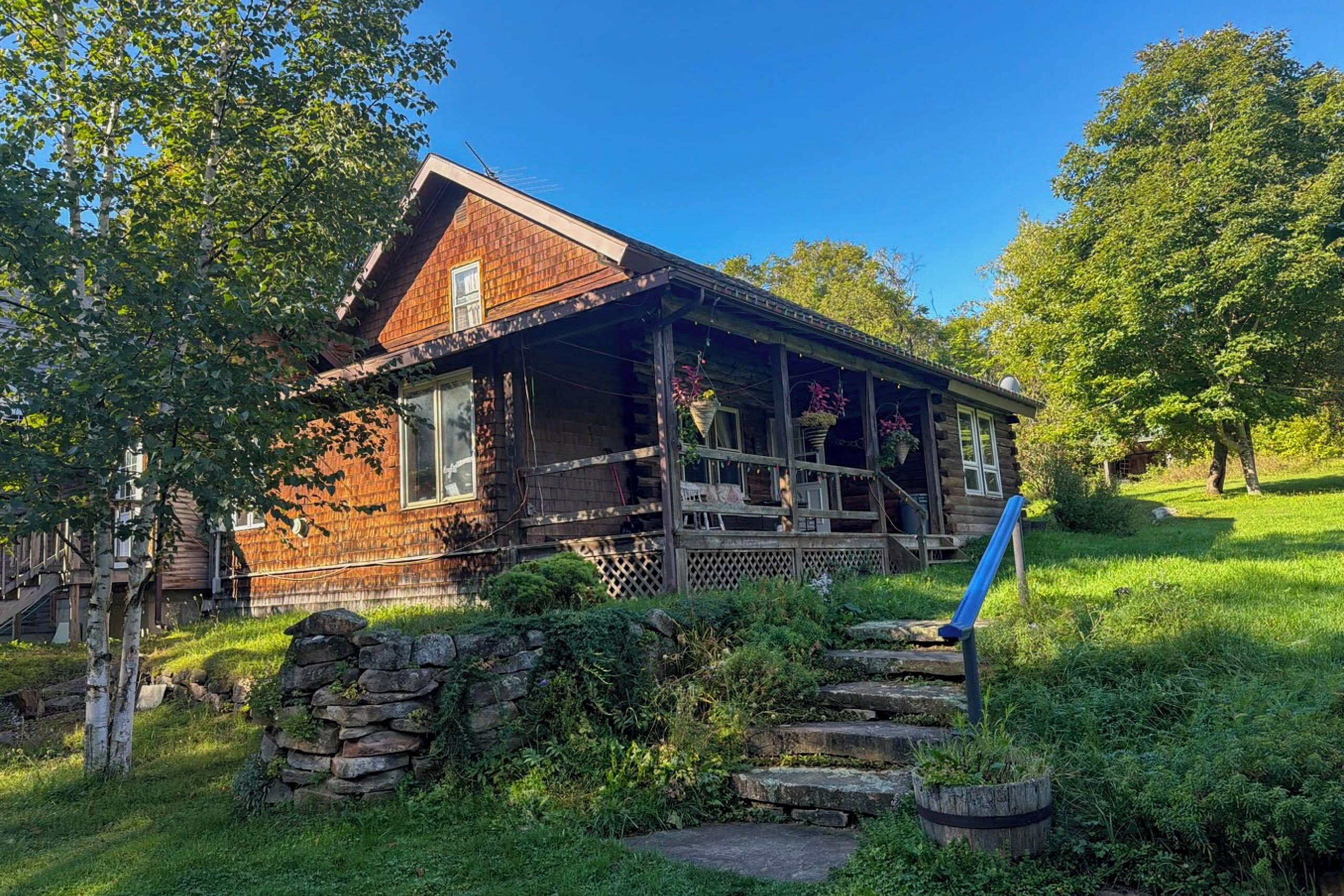 A rustic log cabin with a wooden porch, stone steps, and a stone wall.