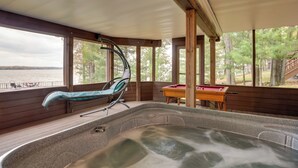 Un jacuzzi en una habitación de madera con ventanas amplias, una mesa de billar y una silla.