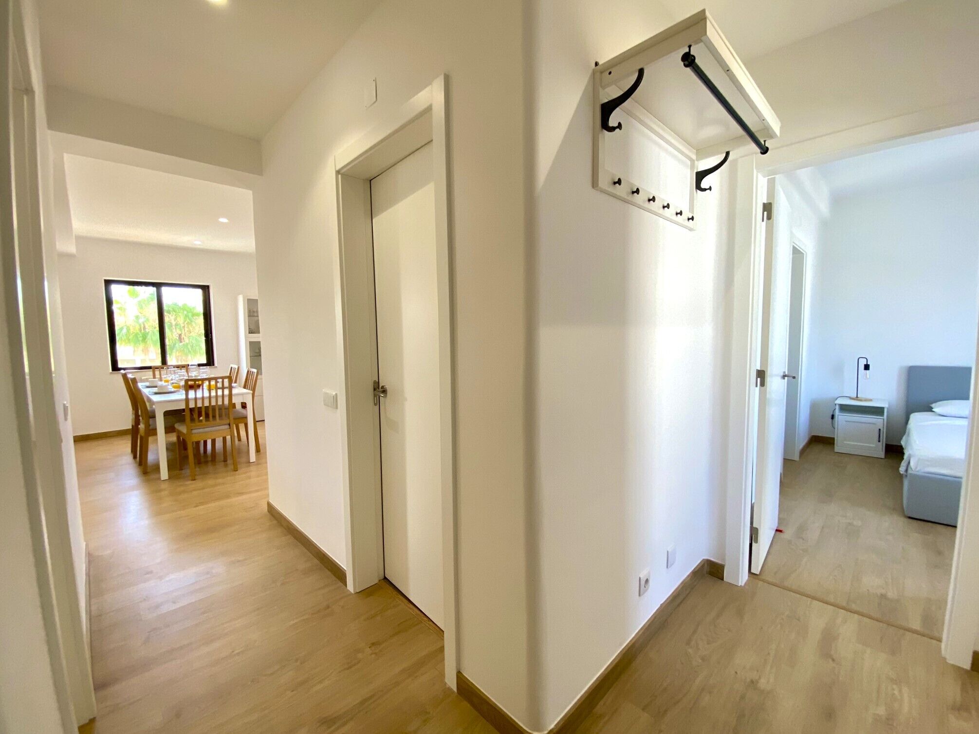 Ein heller, moderner Flur mit Holzboden, der in einen Essbereich mit Tageslicht und ein Bett mit Nachttisch führt.
