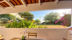 A wooden bench with a potted orchid and a chair, overlooking a garden with various plants and a stone wall. - Albufeira Harmony With Pool by Homing (Albufeira)