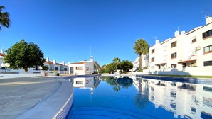 A swimming pool with clear blue water, surrounded by white buildings with red-tiled roofs and palm trees. - Albufeira Harmony With Pool by Homing (Albufeira)