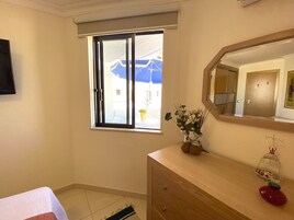 Una habitación con puerta corrediza de vidrio, cómoda de madera, espejo y una pequeña jaula de pájaros.