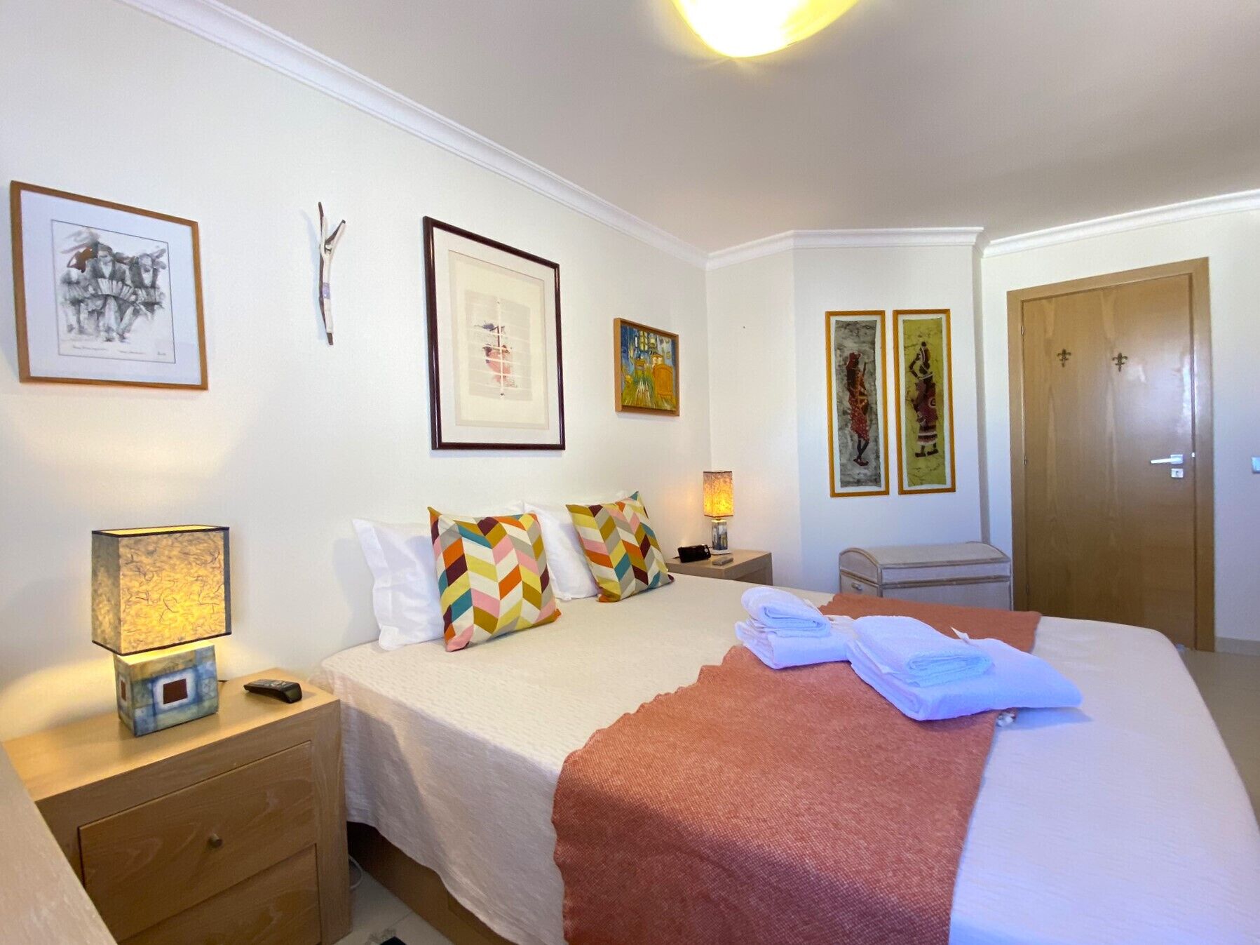 A hotel room with a bed, a nightstand, a lamp, and artwork on the walls.
