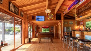 A wooden bar area with a pool table, bar stools, and a neon sign.