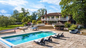 A swimming pool with lounge chairs, a covered seating area, and a house with a balcony.