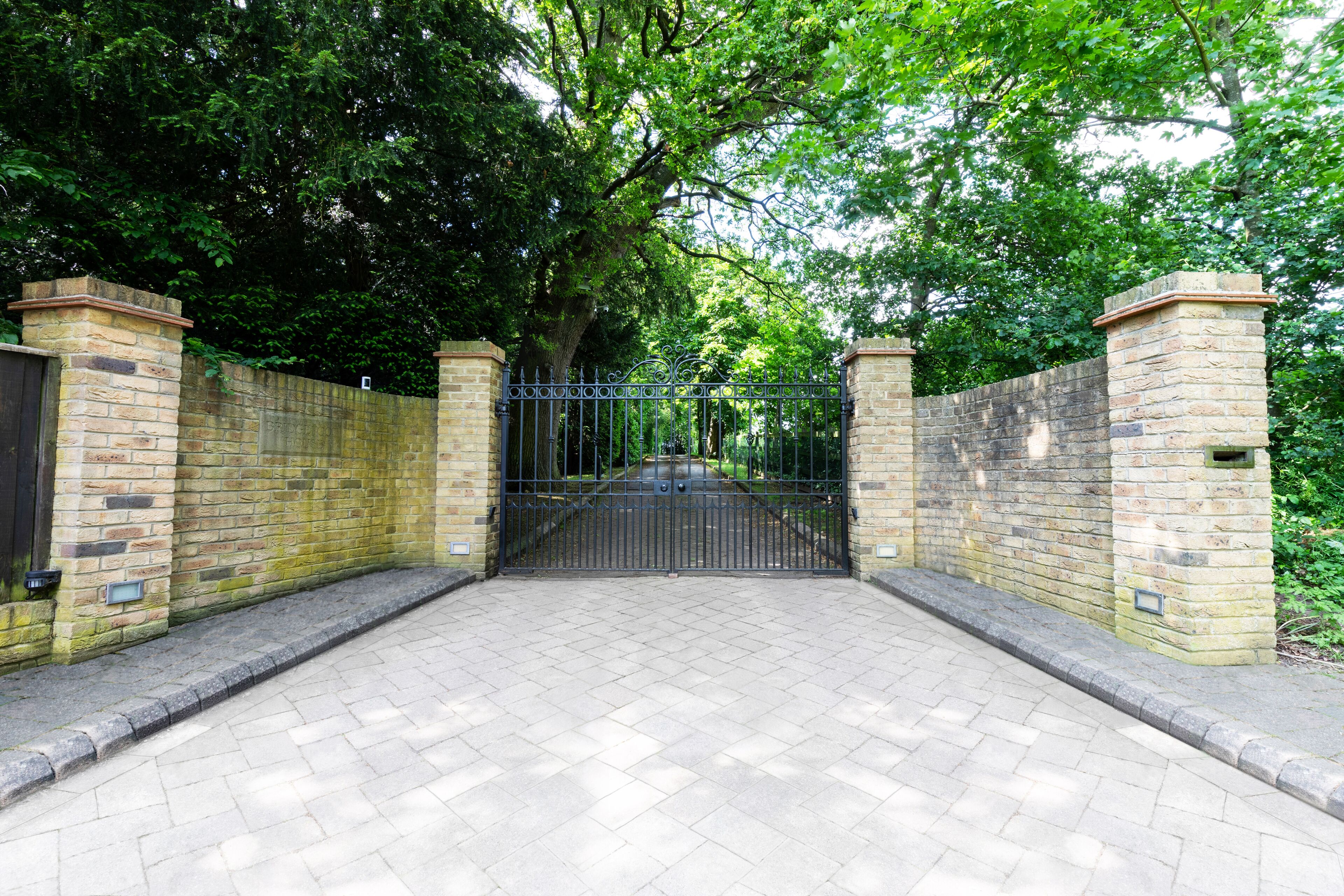 Een omheind toegangspunt met een bakstenen muur en een metalen poort, omringd door bomen.