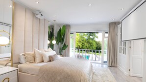 A bedroom with a large bed, a bedside table, a mirror, and a view of a balcony with a pool.
